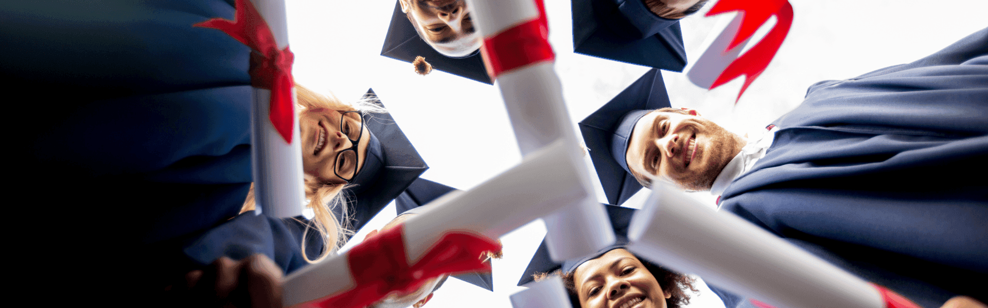 Junge Absolventinnen und Absolventen im Talar blicken lachend mit Abschlussurkunden in den Händen in die Kamera – Symbol für erfolgreichen Studienabschluss und Karrierestart.