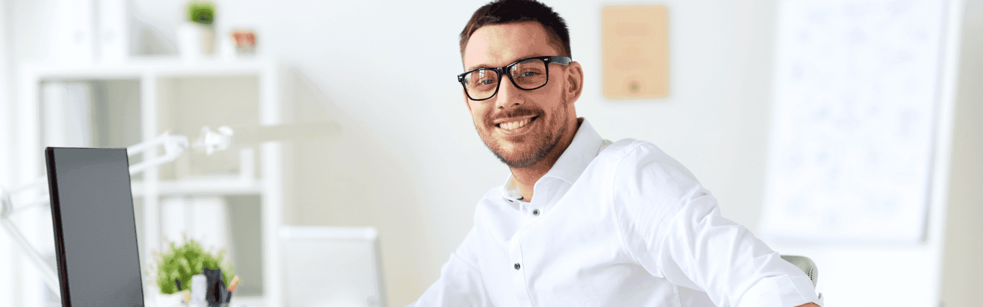 junger Büromitarbeiter sitzt am PC und lächelt seitlich in die Kamera